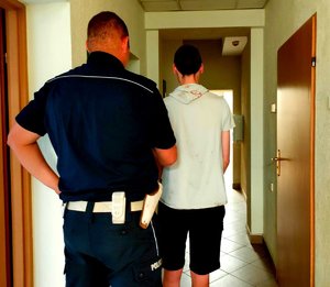 Policjant w mundurze trzymający mężczyznę.