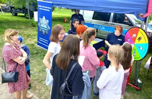 Dzieci stojące przed namiotem policjantki w mundurach przeprowadzają gry i zabawy z nimi.