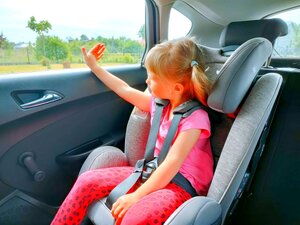 Dziewczynka siedząca w foteliku samochodowym w aucie, rączkę przykłada do szyby.