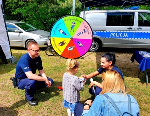 Policjanci w mundurach kucają przy dziecku, w tle radiowóz.