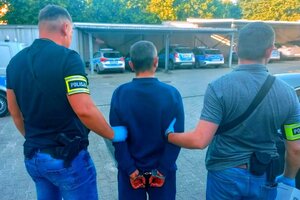 Policjanci nieumundurowani trzymający zatrzymanego mężczyznę, na rękach mają opaski z napisem policja.