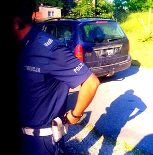policjant w mundurze i samochód stojąy na drodze