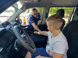 Policjant zakłada na rękę odblask chłopcu siedzącemu w radiowozie.