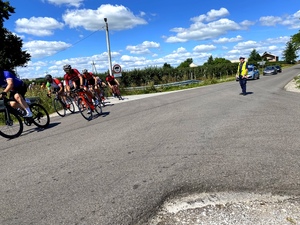 Policjant stojący w umundurowaniu na skrzyżowaniu, obok przejeżdżają rowerzyści.