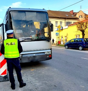 Policjant w kamizelce odblaskowej z napisem policja stojący tyłem i autokar.