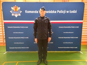 Policjant w mundurze na tle tablicy z napisem Komenda Wojewódzka Policji w Łodzi.