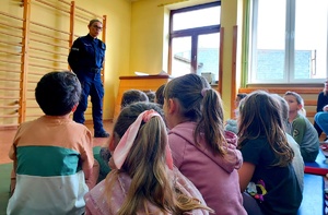 Policjantka w mundurze rozmawia z małymi dziećmi siedzącymi przed nią.