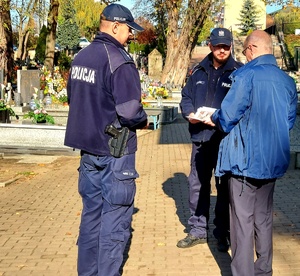 Policjanci rozmawiają z mężczyznę na cmentarzu.