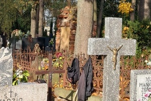 Wiszący otwarty plecak i kurtka na ogrodzeniu przy grobie.