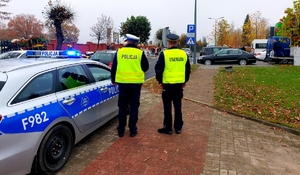 Policjant i strażnik miejski stoją przy radiowozie.