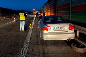 Policjant w kamizelce z napisem policja w trakcie oględzin i pojazd stojący na pasie awaryjnym, z tyłu auta leży koło zapasowe.