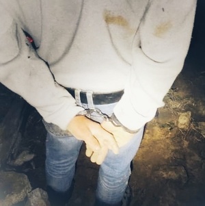 Mężczyzna stojący tyłem przy wodzie , ma na rękach kajdanki.