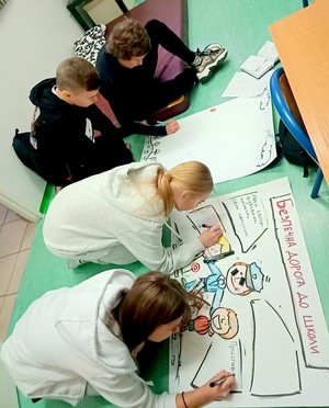 Młodzież klęcząca na podłodze i rysująca plakaty profilaktyczne wraz z opisami po ukraińsku.