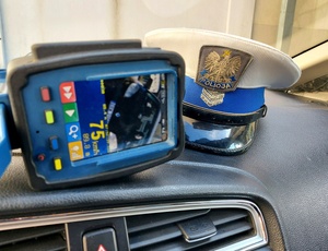 Czapka policyjna na podszybiu radiowozu oraz miernik prędkości.