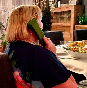 kobieta siedząca przy stole i trzyma słuchawkę telefonu przy uchu.