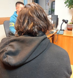 mężczyzna siedzący tyłem, przy biurko policjant przesłuchujący go.