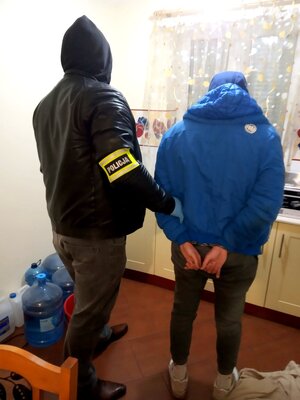 policjant nieumundurowany z opaska z napisem policja trzyma zatrzymanego mężczyznę.