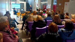 policjantka w mundurze stojąca przed rodzicami siedzącymi na krzesłach.