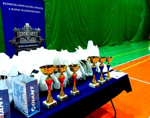 puchary i nagrody stojące na stole w tle napis komenda powiatowa policji w rawie i gwiazda policyjna.