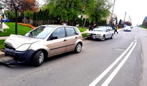 dwa pojazdy rozbite stojące na poboczu drogi, policjant idące po drodze w kamizelce odblaskowej i w oddali radiowóz.