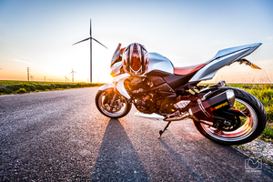 motocykl zaparkowany na drodze w tle zachód słońca i wiatrak.