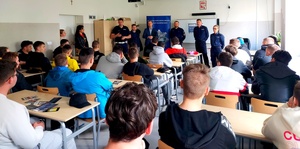 policjanci i goście stojący przed młodzieżą siedzącą w ławkach.