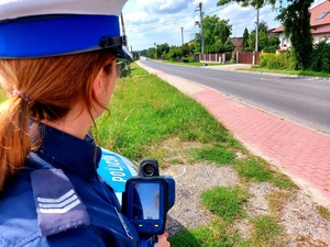 policjantka stojąca z miernikiem prędkości przy drodze.