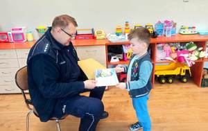 policjant wręcza dziecku książeczkę.