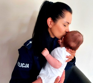 policjantka w mundurze całuje w główkę trzymające niemowlę w rekach.