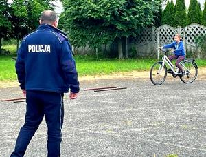 Policjant w mundurze patrzy jak dziewczynka na rowerze pokonuje tot przeszkód.