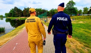 policjant i strażak idą chodnikiem wzdłuż zalewu.