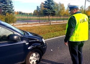 Policjant stojący przy uszkodzonym aucie.