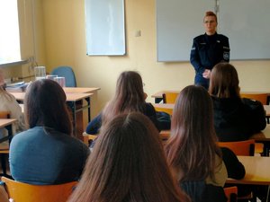 Policjantka stojąca przed młodzieżą siedzącą w ławkach.