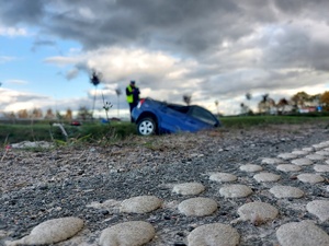 Policjant stojący przy aucie leżącym w rowie.