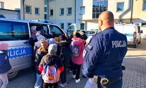 Policjant i dzieci z plecakami wsiadające do radiowozu.