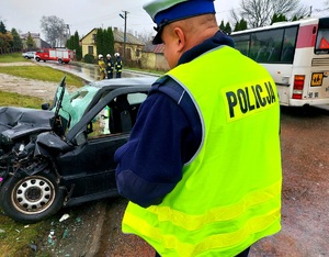 Policjant stojący tyłem przy rozbitym aucie.