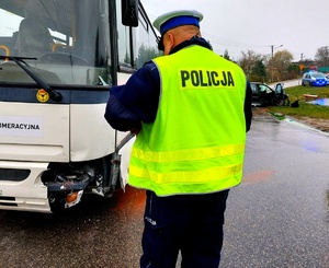 Policjant stojący tyłem przy uszkodzonym autobusie.