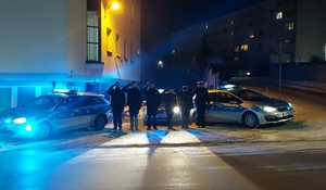Policjanci oddający hołd, salutują. obok radiowozy ż włączonymi światłami błyskowymi.