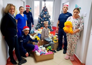 Policjanci, pielęgniarki i dzieci z oddziału przy zabawkach pod choinką.