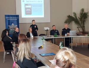Policjantka mówiąca przez mikrofon i inne siedzące przy stole.