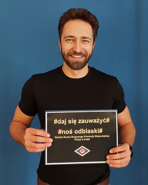Mężczyzna trzymający kartkę w ręce z napisem daj się zauważyć noś odblaski.