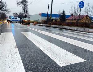 Przejście dla pieszych, auto stojące za przejściem, radiowóz z włączonymi światłami błyskowymi.