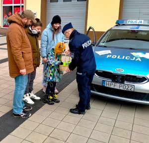 Policjantka daje odblaski dorosłym i dzieciom obok radiowóz.