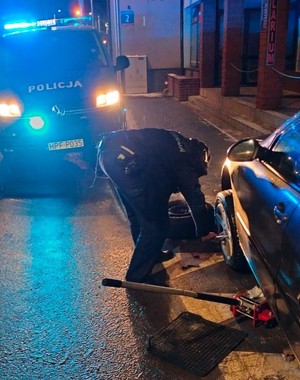Policjant schylony podczas wymiany koła w samochodzie a tle radiowóz policyjny.