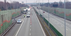 Samochody na drodze dwupasmowej, radiowóz oraz dwóch policjantów.