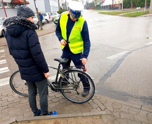 Policjant rozmawia z rowerzystą i przekazuje odblask.
