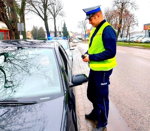 Policjant rozmawia z kierującą siedzącą w aucie.