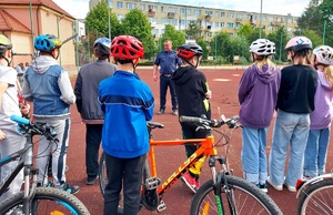 Dzieci w kaskach stojące z rowerami a przed nimi policjant.