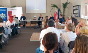 Osoby siedzące przy stołach o prelegenci rozmawiający przez mikrofon.