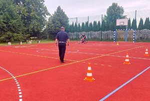 Policjant i dziecko jeżdżące na rowerze po boisku.